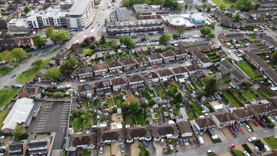 An aerial view of a residential neighborhood with a mixture of terraced houses and semi-detached homes, each with small, well-maintained gardens and varied roofing materials including tiled and flat r